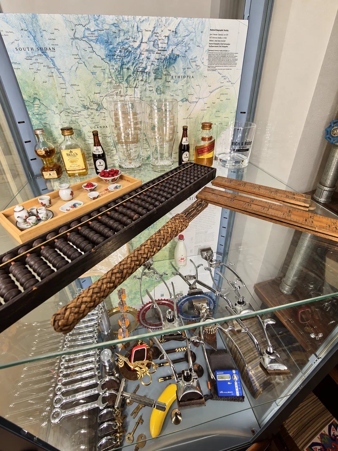 Display case with miniature spirits, a wooden abacus, teacups and an old wall map, arranged like a curiosity cabinet.