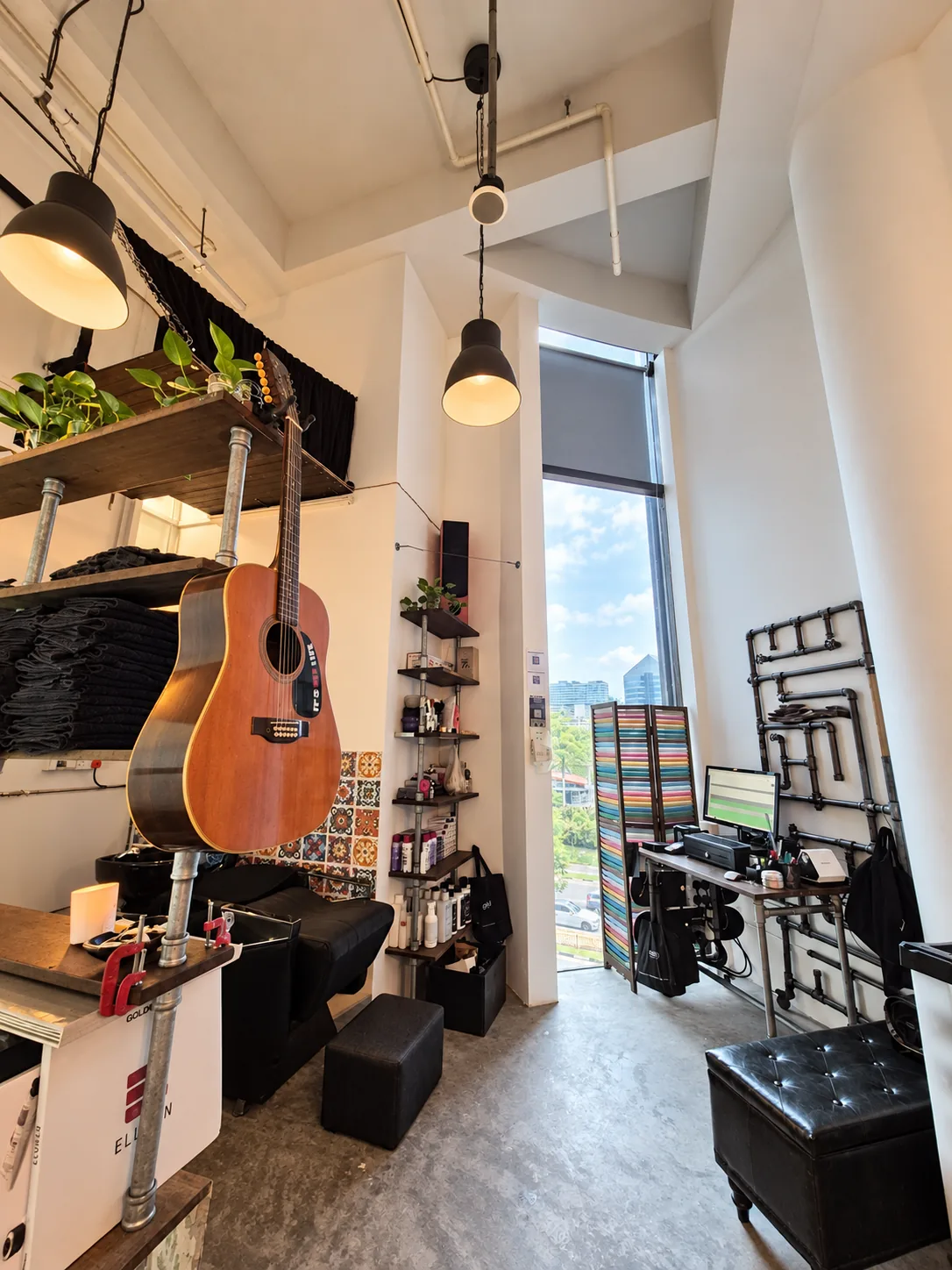 An acoustic guitar hanging within reach of the wash basin, with shelving and a tall window looking out over the city.
