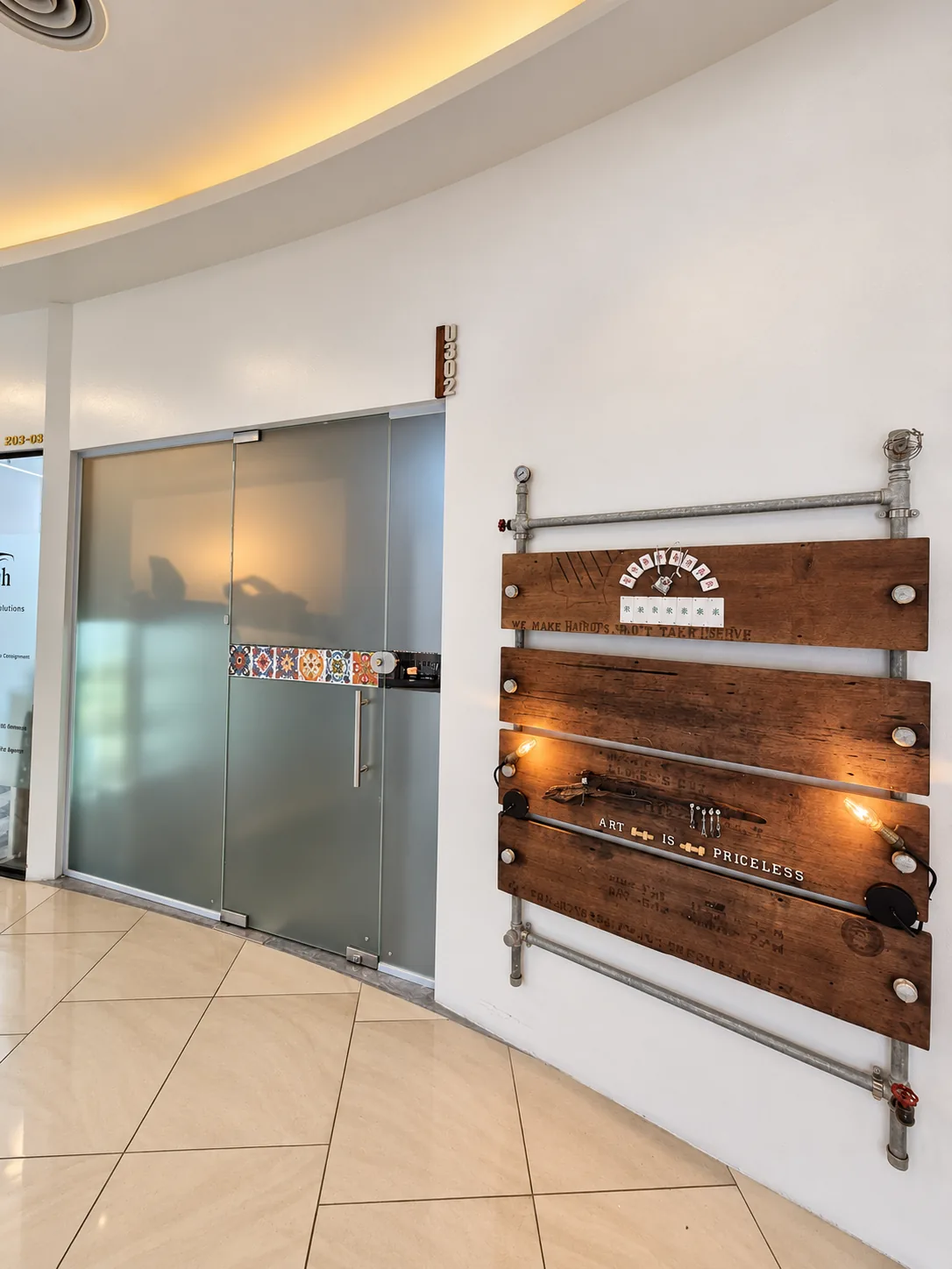 Reclaimed timber signage mounted on plumbing pipe outside the studio door, hand-lettered with the shop's motto.