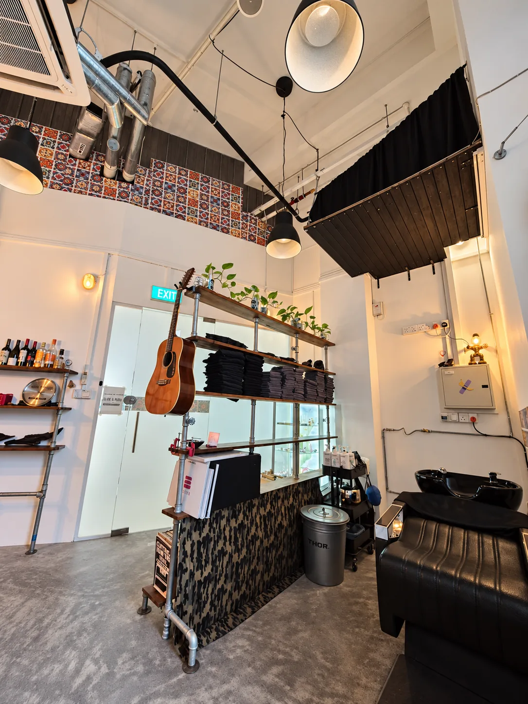 Guitar hanging beside the wash station, with a wooden shelf of folded gowns and a view of the Singapore skyline through the studio window.